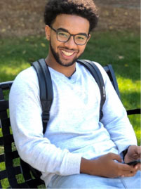 Mustafa Saaed sitting on a bench. Wearing white. Grass background.